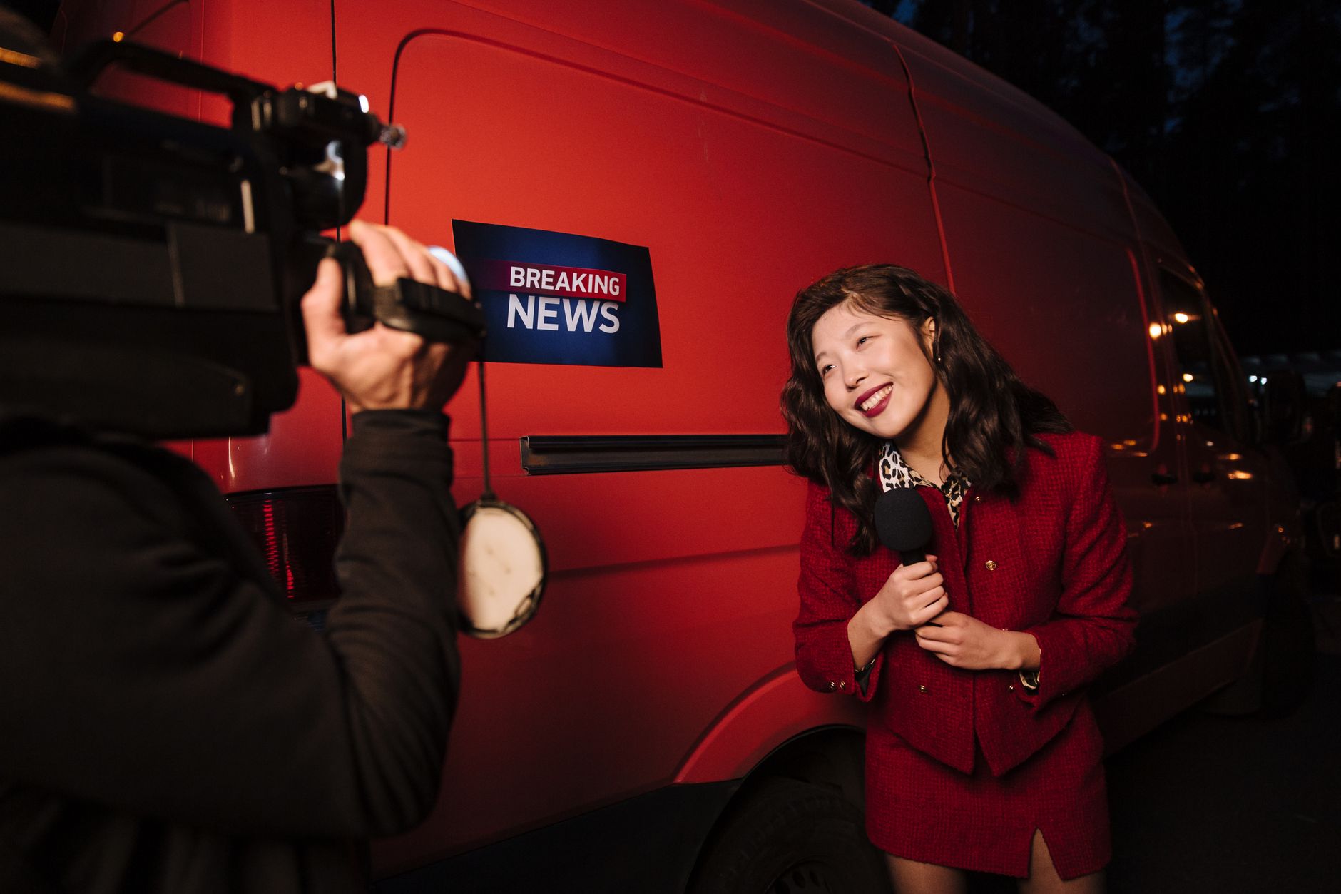 Asian female reporter in a red blazer reporting live on the news outdoors in the evening. — Wie integriert LuckyGem Casino ne